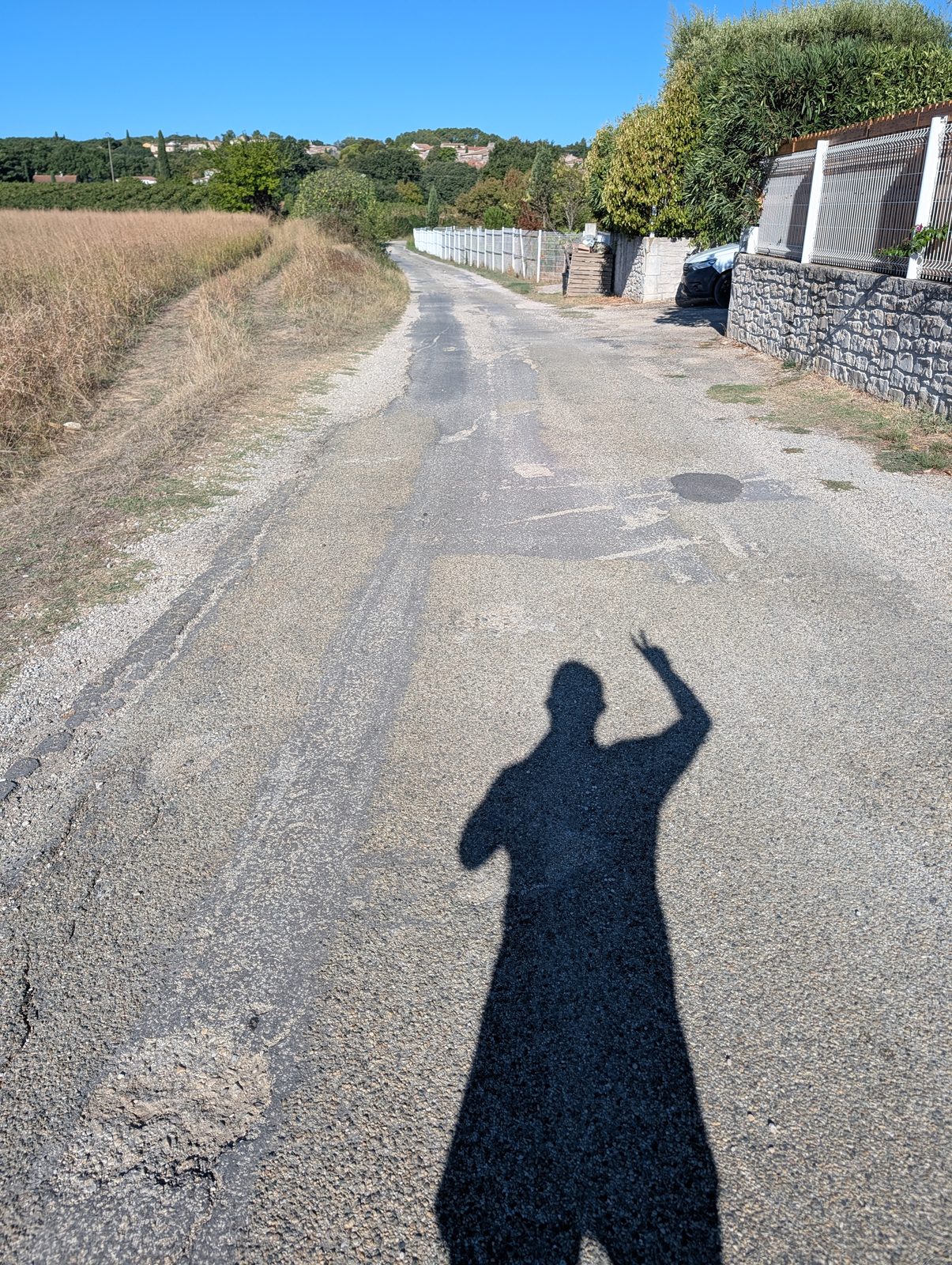 Ombre du coureur sur une petite route de campagne, bras levé, en fin de sortie sous un ciel bleu.