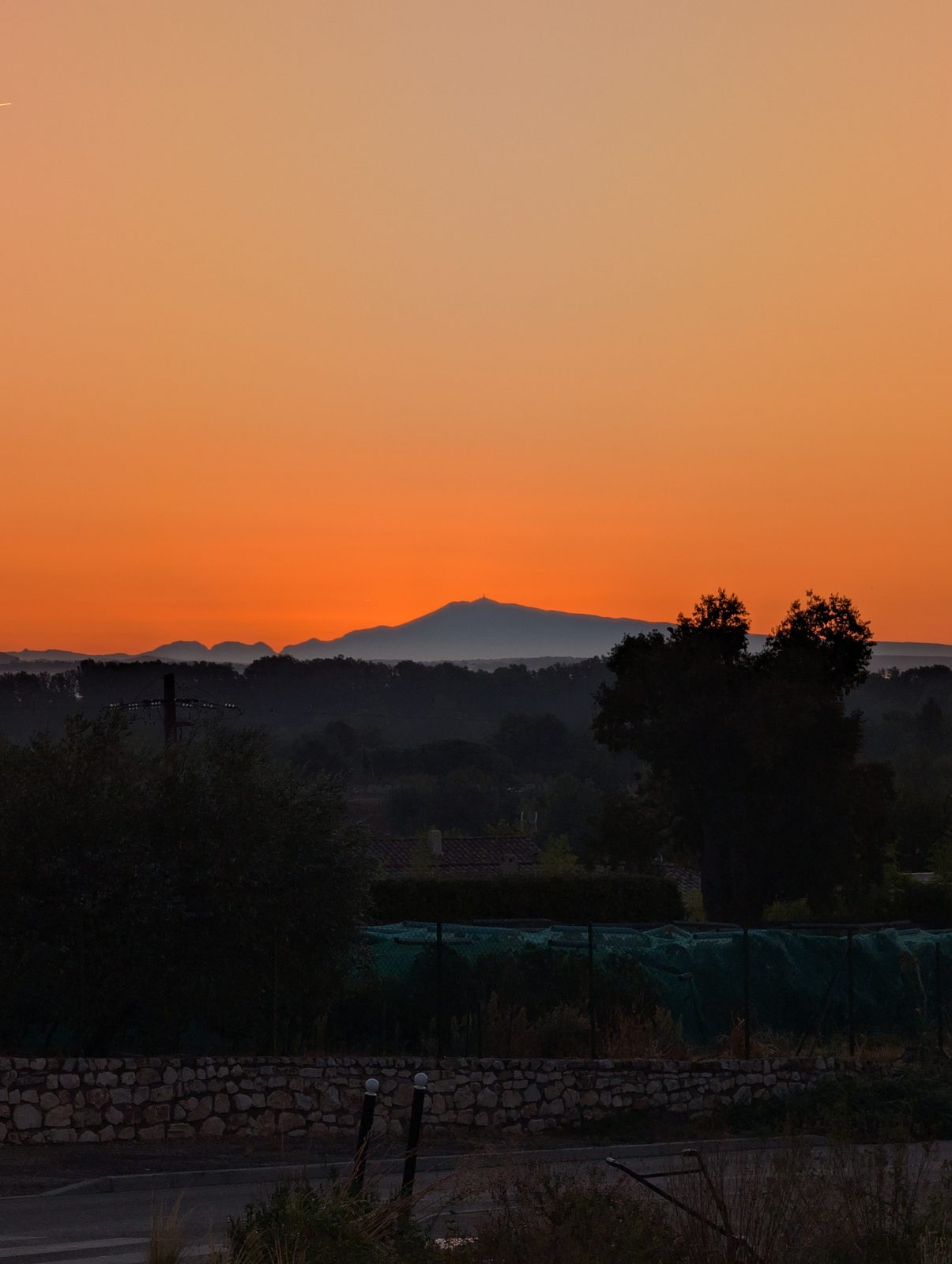 Lever de soleil orange sur la plaine, le mont Ventoux se détachant en silhouette bleue à l&rsquo;horizon.